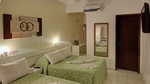 A hotel room with two beds, each with a green floral bedspread and white pillows. There is a wall-mounted artwork above the beds, a bedside table with a lamp, and a mirror on the wall. - Foz Presidente Economic Hotel (Foz do Iguaçu)