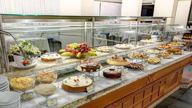 A buffet with various food items and a glass display case. - Foz Presidente Economic Hotel (Foz do Iguaçu)