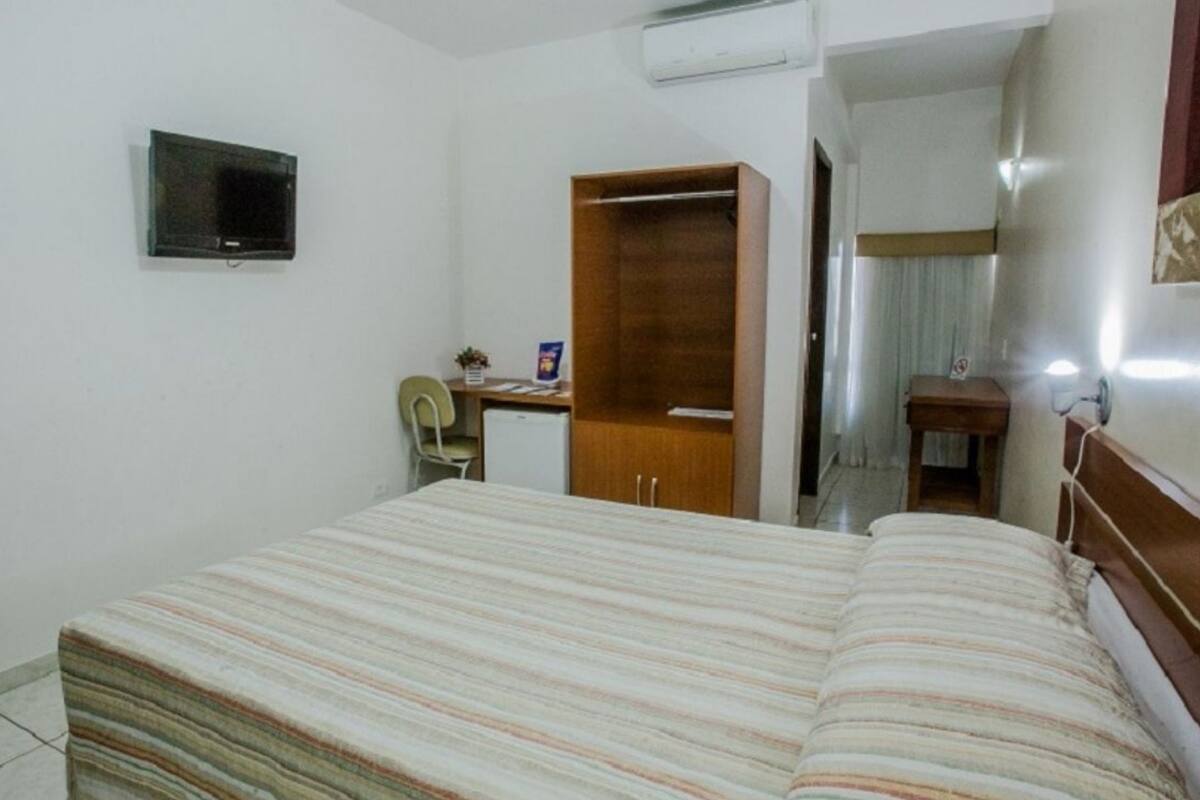 Une chambre d’hôtel comprenant un lit, un bureau avec une chaise, une armoire, une télévision et une petite table avec une lampe.