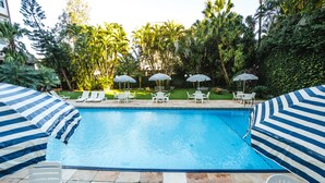 A swimming pool with lounge chairs and umbrellas, surrounded by lush greenery. - Foz Presidente Economic Hotel (Foz do Iguaçu)