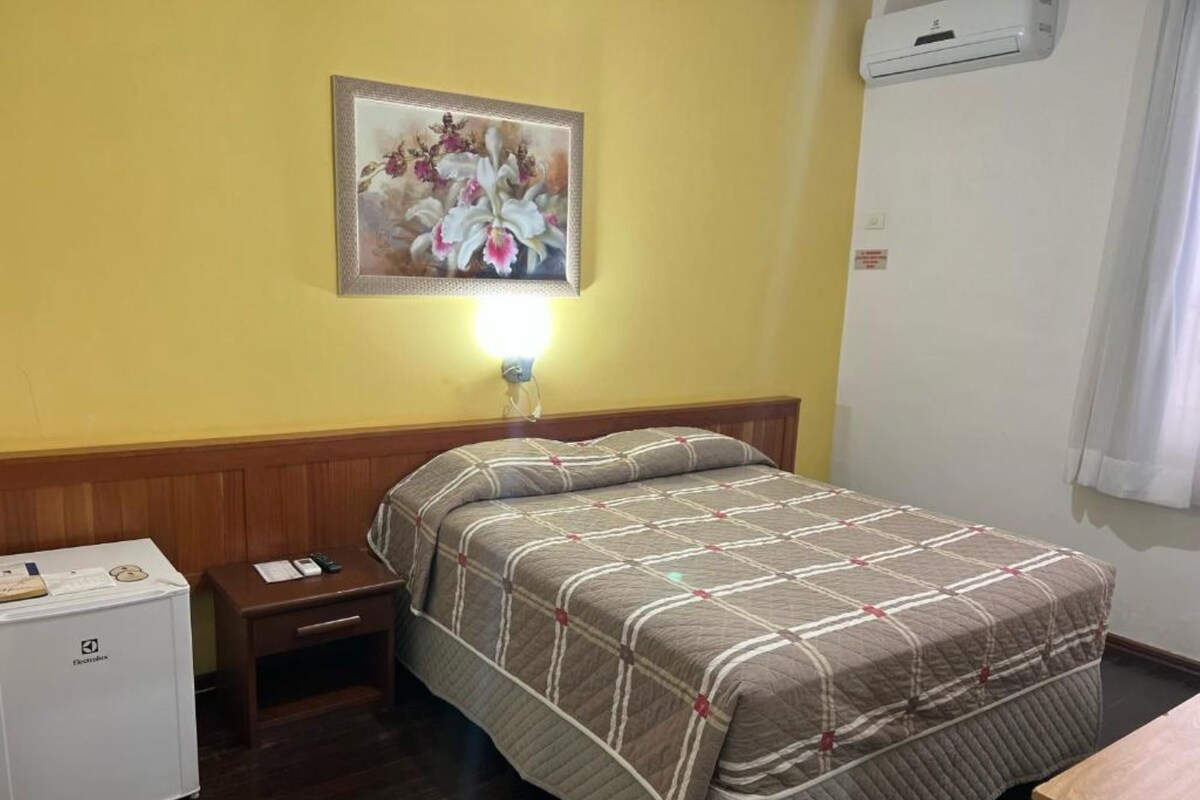 A hotel room with a bed, bedside table, and a small refrigerator.