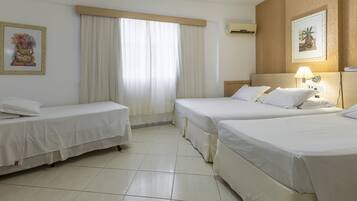 Une chambre d’hôtel avec deux lits simples, une grande fenêtre avec des rideaux, un climatiseur fixé au mur et des œuvres d’art encadrées.
