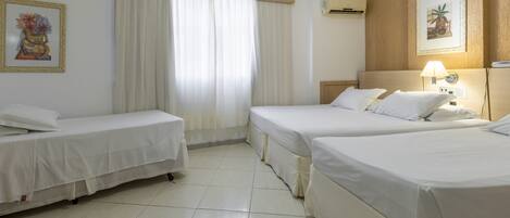 Habitación de hotel con dos camas individuales, un ventanal con cortinas, aire acondicionado instalado en la pared y obras de arte enmarcadas.