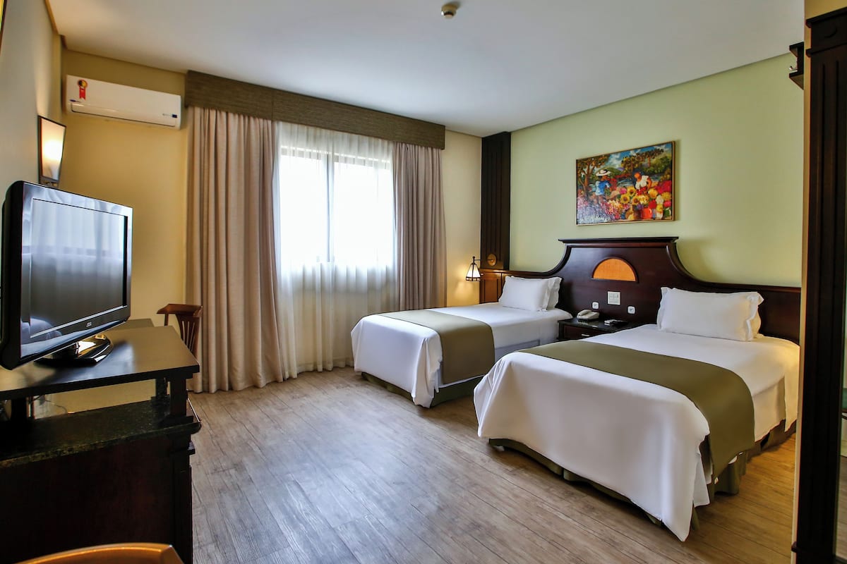 A hotel room with two beds, a TV, a desk, and a painting on the wall.