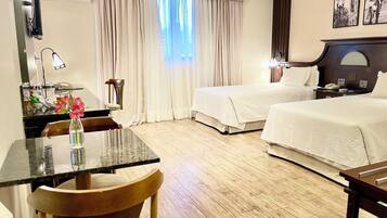 A hotel room with two beds, a desk with a chair, a small table with a vase, and a window with curtains.