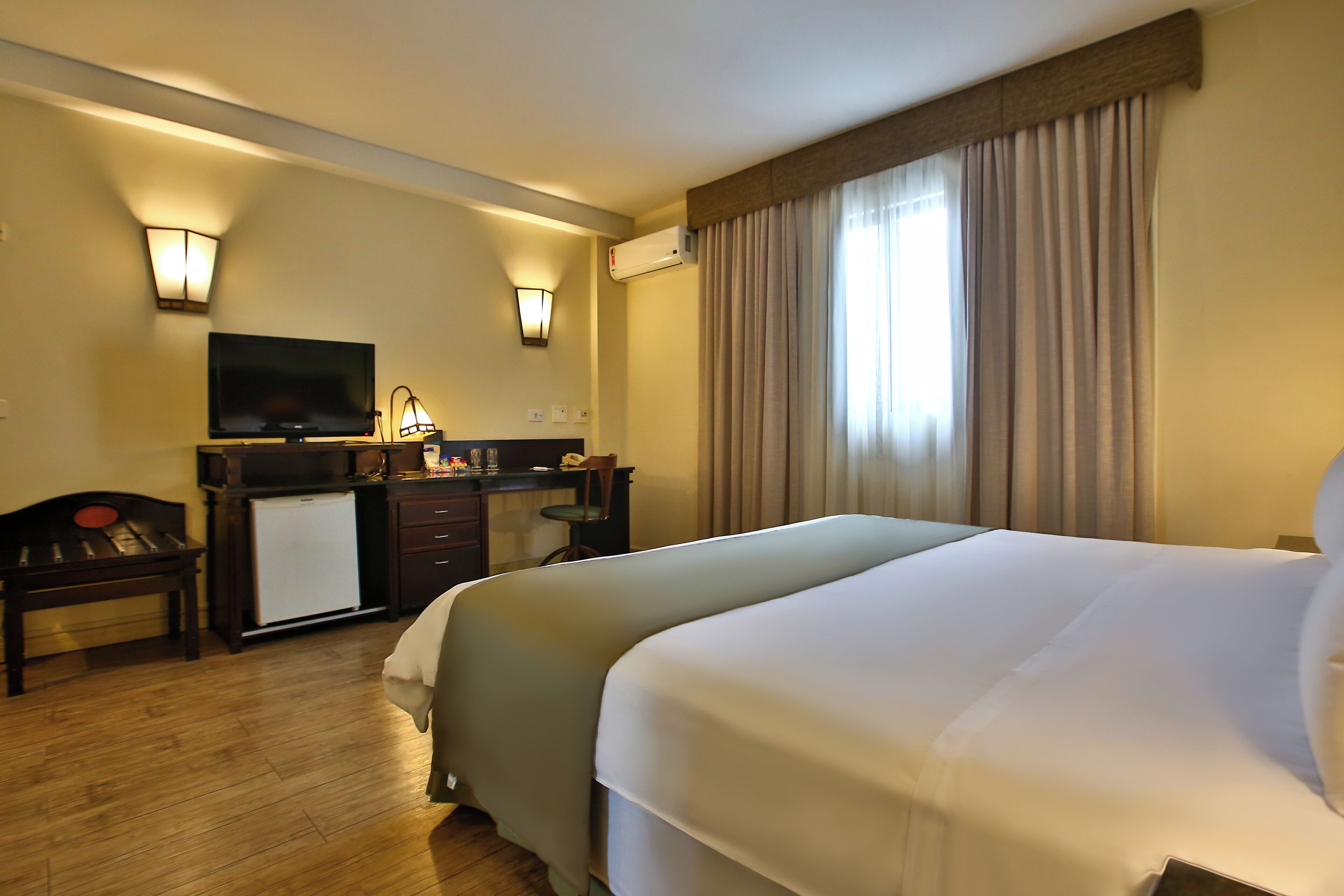 Habitación de hotel con una cama grande, un escritorio con televisor y un minibar.