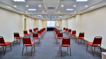 Une salle de conférence avec des rangées de chaises rouges, un écran de projection et un écran de présentation.
