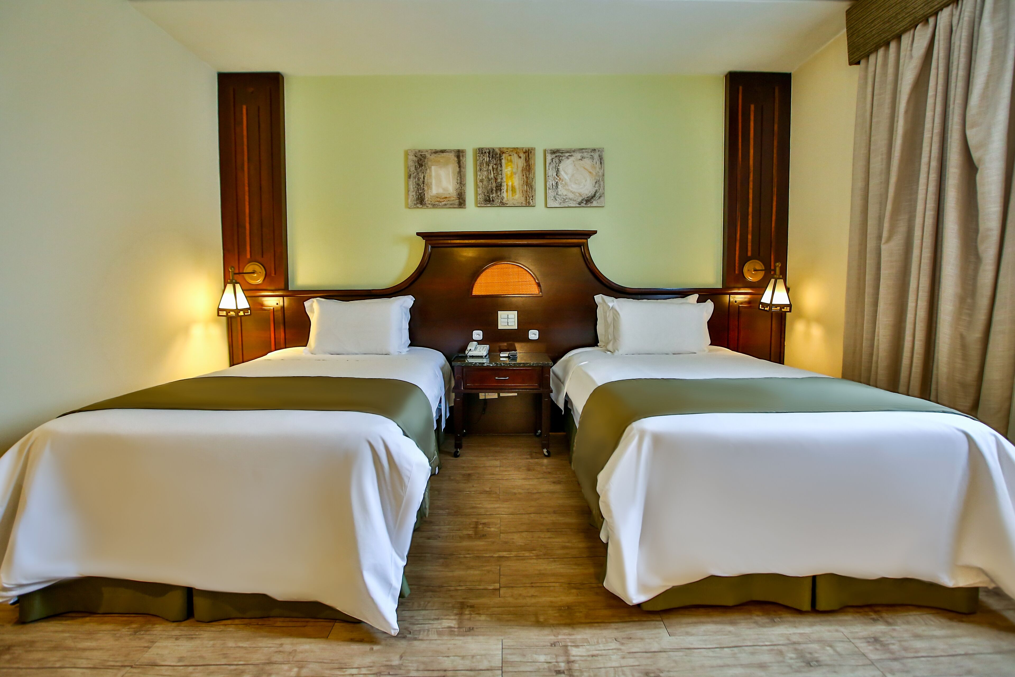 A hotel room with two beds, a wooden headboard, a nightstand, and a wall clock.