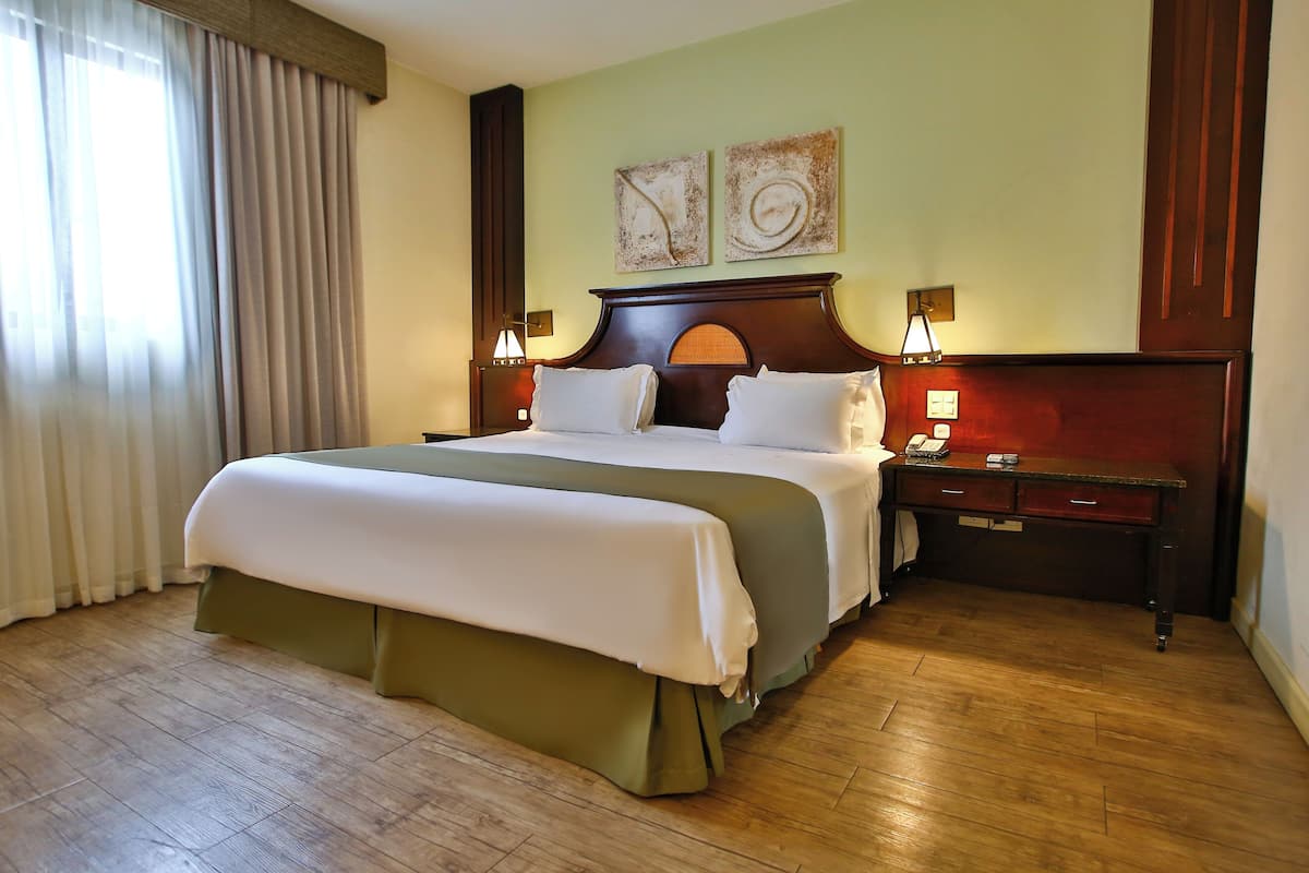 A hotel room with a large bed, wooden floor, two bedside tables with lamps, and artwork on the wall.