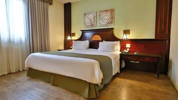 A hotel room with a large bed, wooden floor, two bedside tables with lamps, and artwork on the wall.