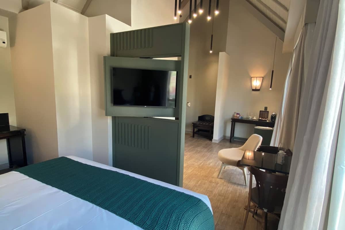 A hotel room with a large bed, a television, a desk with a chair, and a ceiling with exposed beams.