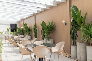 An outdoor patio with round tables and wicker chairs, surrounded by potted plants and a wooden wall. - SLIM Curitiba Alto da XV (Curitiba)