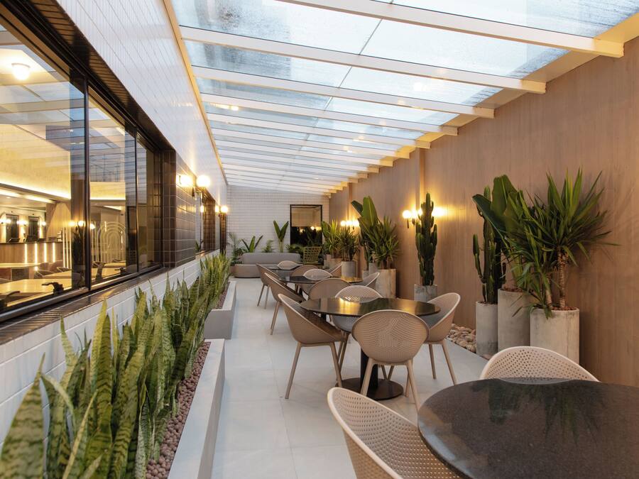 A modern outdoor dining area with glass walls, tables, chairs, and potted plants.