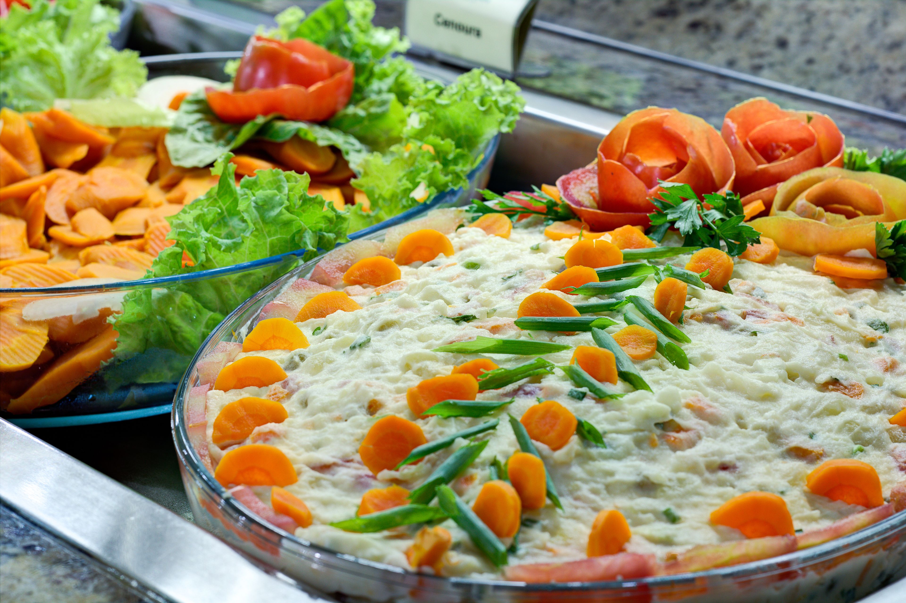 A buffet with various dishes including a creamy dip garnished with carrots and green beans, and other salads with vegetables.