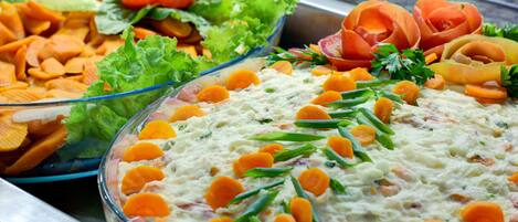 A buffet with various dishes including a creamy dip garnished with carrots and green beans, and other salads with vegetables.