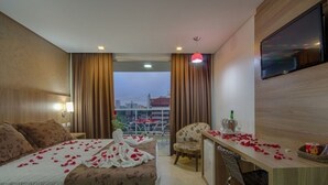 Hotelkamer met een bed, bureau, stoel, televisie en een balkon met gordijnen.
