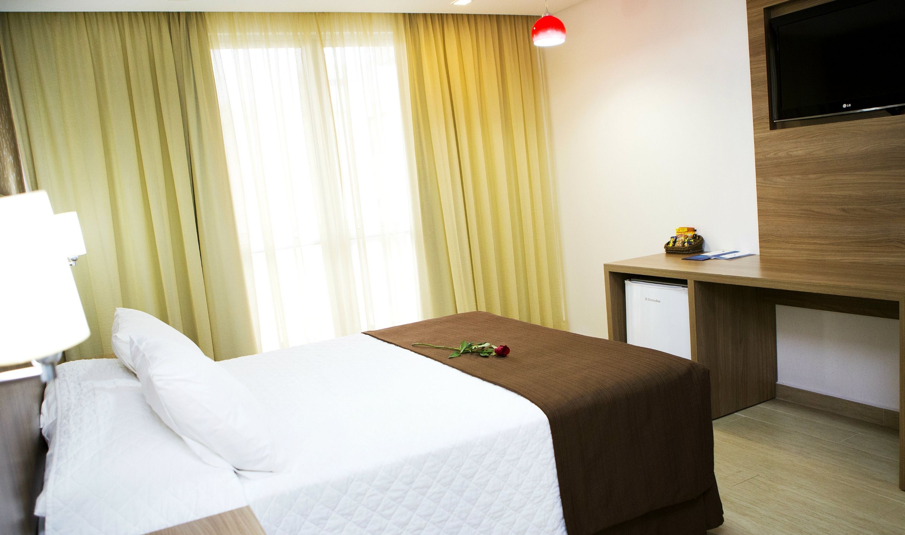 A hotel room with a bed, a desk, a television, and a window with curtains.