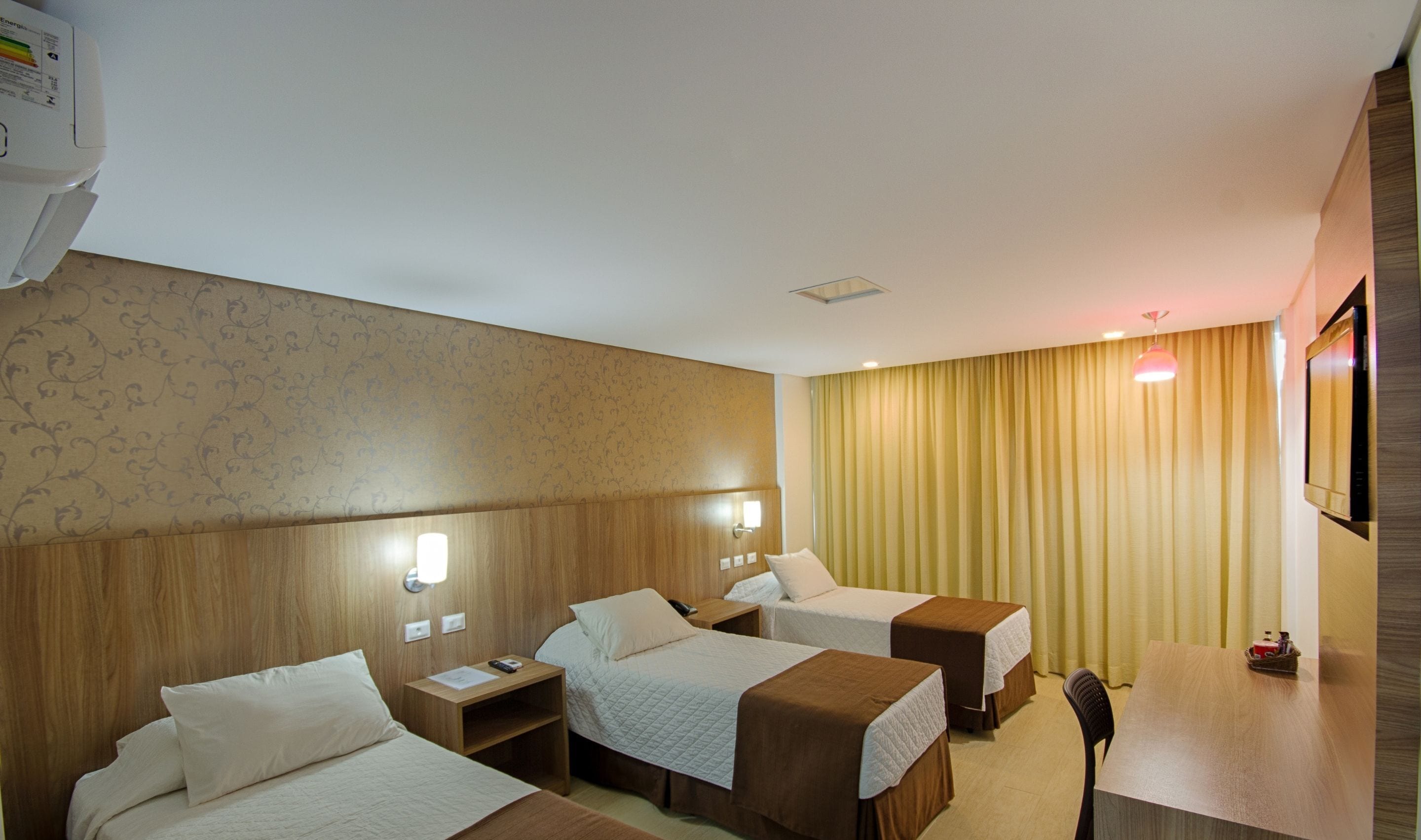 A hotel room with three beds, a desk, and a TV.