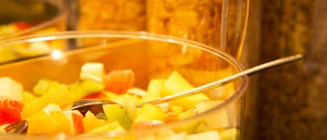 A close-up of a fruit salad with a spoon in a glass bowl.