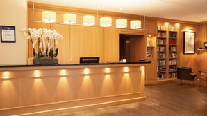 Een hotel receptie met een houten balie, een potorkidee, een boekenplank en een ingelijste foto aan de muur.
