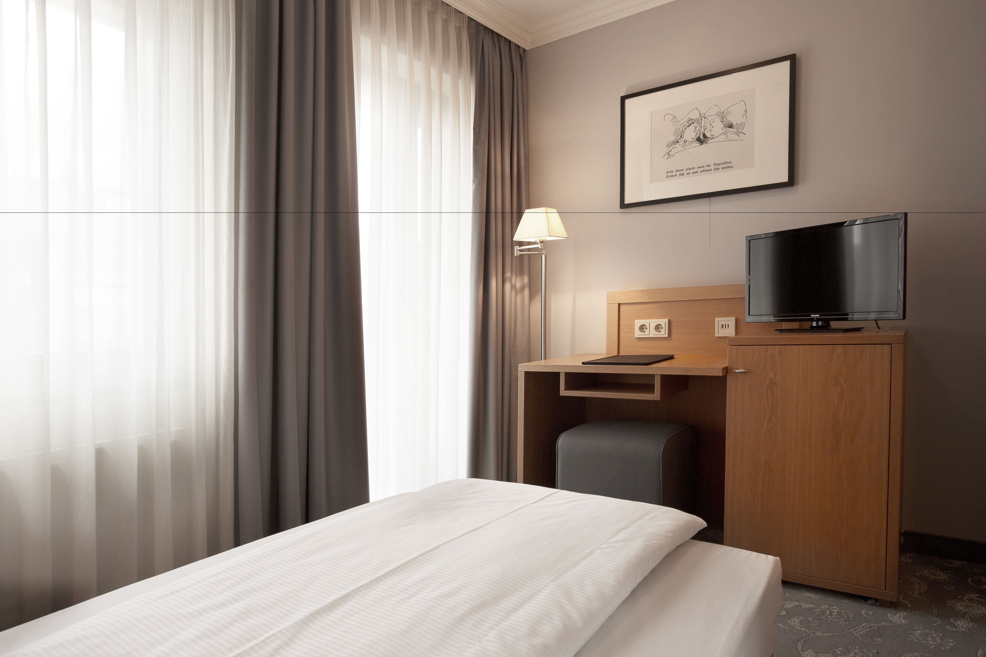 A hotel room with a bed, a desk with a chair, a television, and a framed picture on the wall.