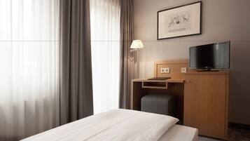 A hotel room with a bed, a desk with a chair, a television, and a framed picture on the wall.