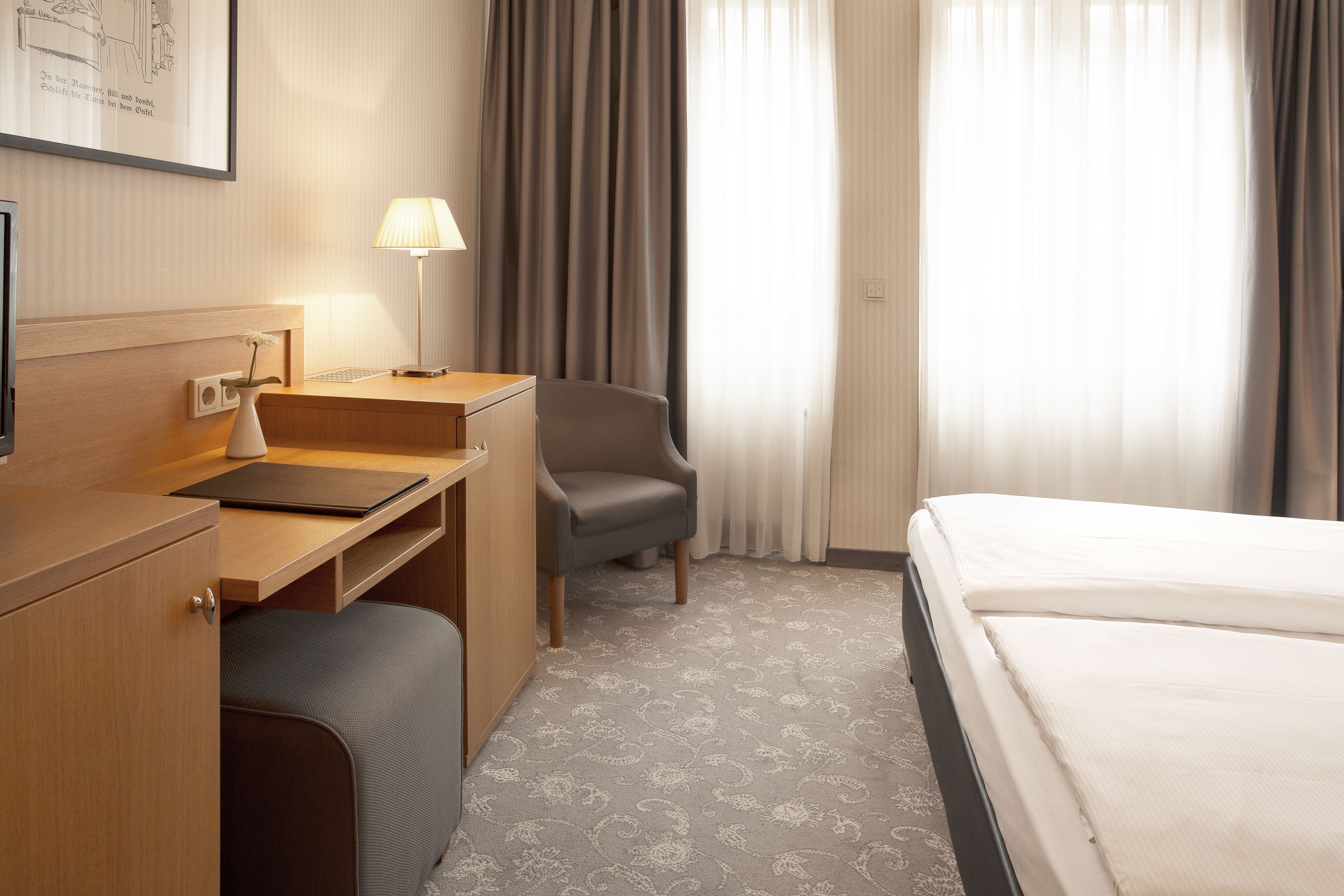 A hotel room with a bed, a desk, a chair, a lamp, and a window with curtains.