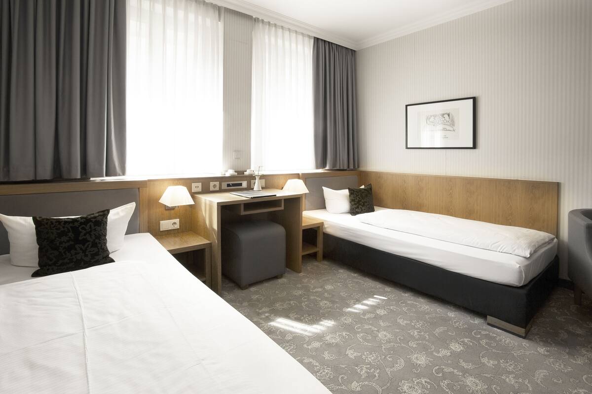 Een hotelkamer met een bed, bureau, stoel, een klein tafeltje en een raam met gordijnen.