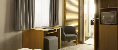 A hotel room with a bed, desk, chair, TV, and a wardrobe.