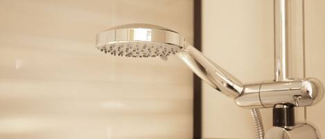 Une pomme de douche chromée, dotée d’un flexible, est fixée au mur, qui est recouvert de carreaux.