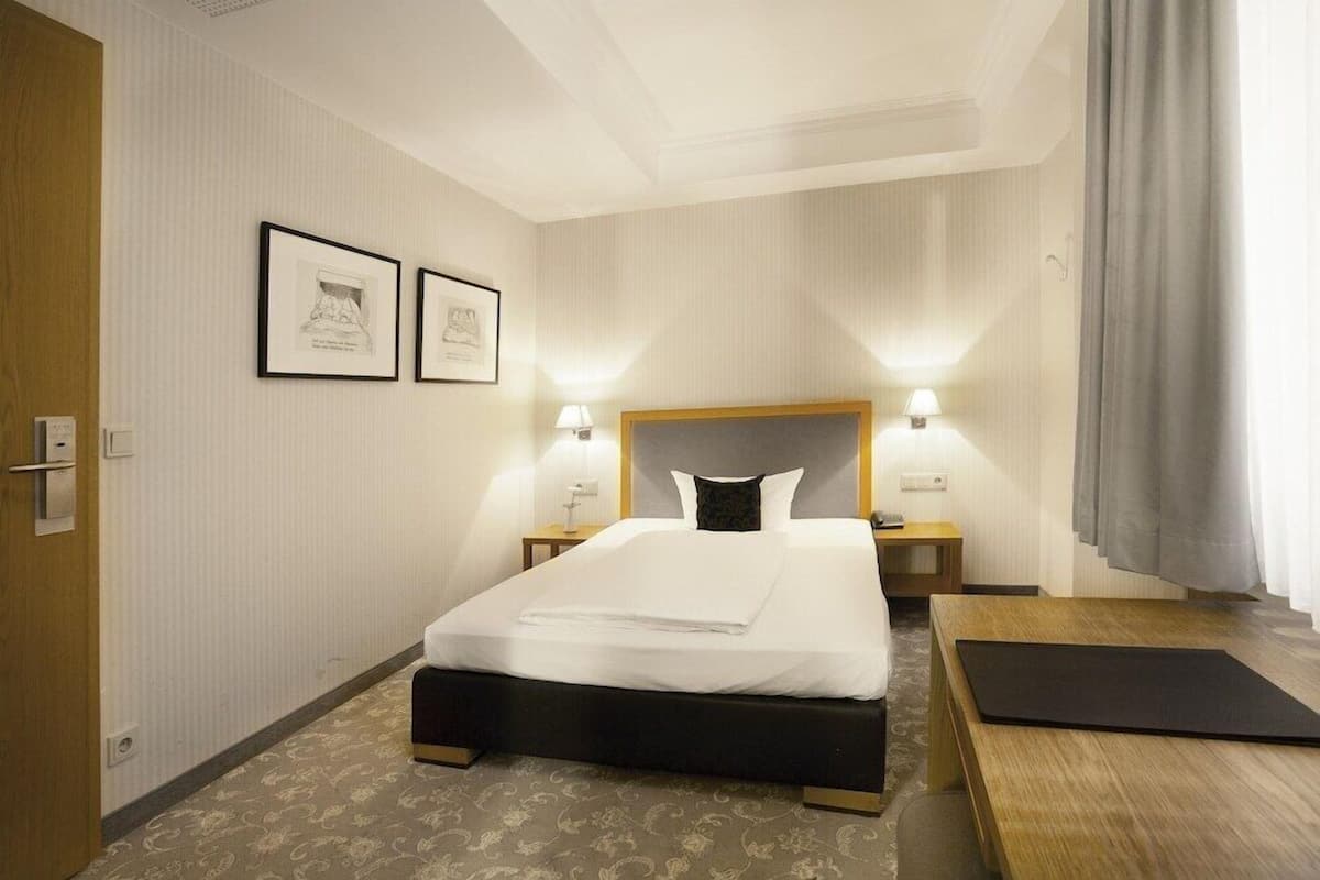 Een hotelkamer met een bed, nachtkastjes, een bureau en een raam met gordijnen.