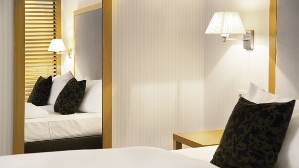 Een hotelkamer met een bed, nachtkastje, lamp en spiegel.