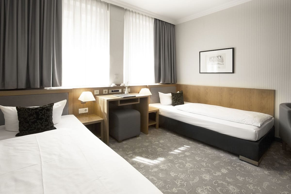 Een hotelkamer met een bed, bureau, stoel en een klein pouf.