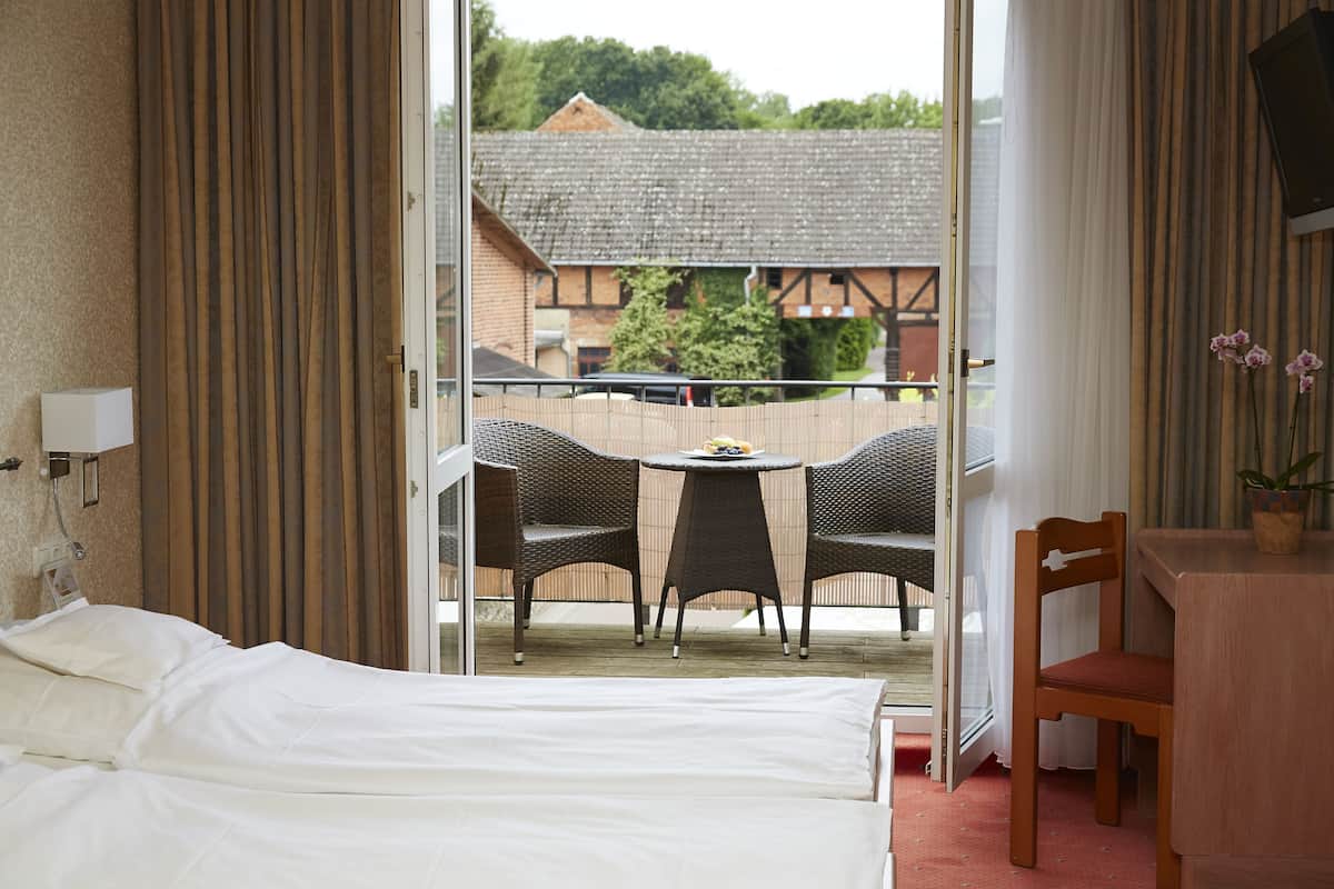 Une chambre d’hôtel avec un lit, une petite table et des chaises, et une vue sur un immeuble et des arbres à l’extérieur.