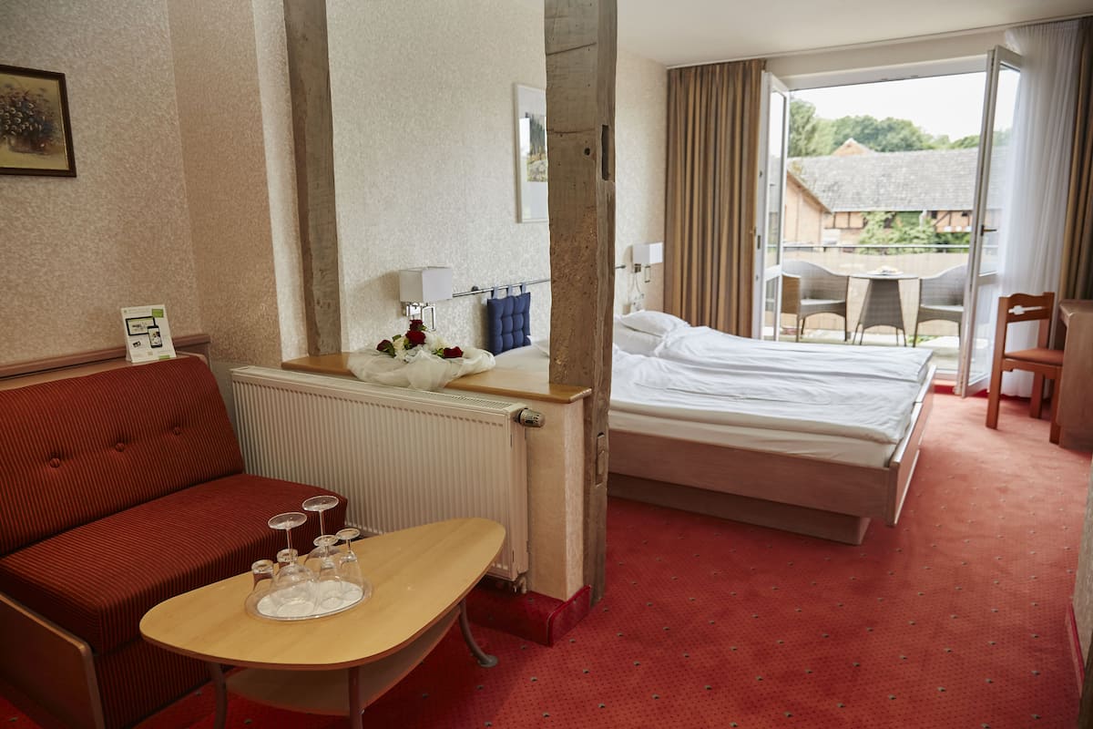 Une chambre d’hôtel avec un lit, un canapé rouge, une petite table sur laquelle se trouve un plateau avec des verres, un radiateur et une vue sur l’extérieur.