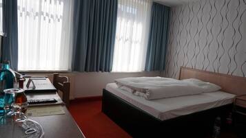 A hotel room with a bed, a desk with a laptop, a chair, and a window with curtains.