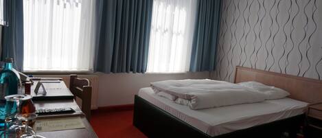 A hotel room with a bed, a desk with a laptop, a chair, and a window with curtains.
