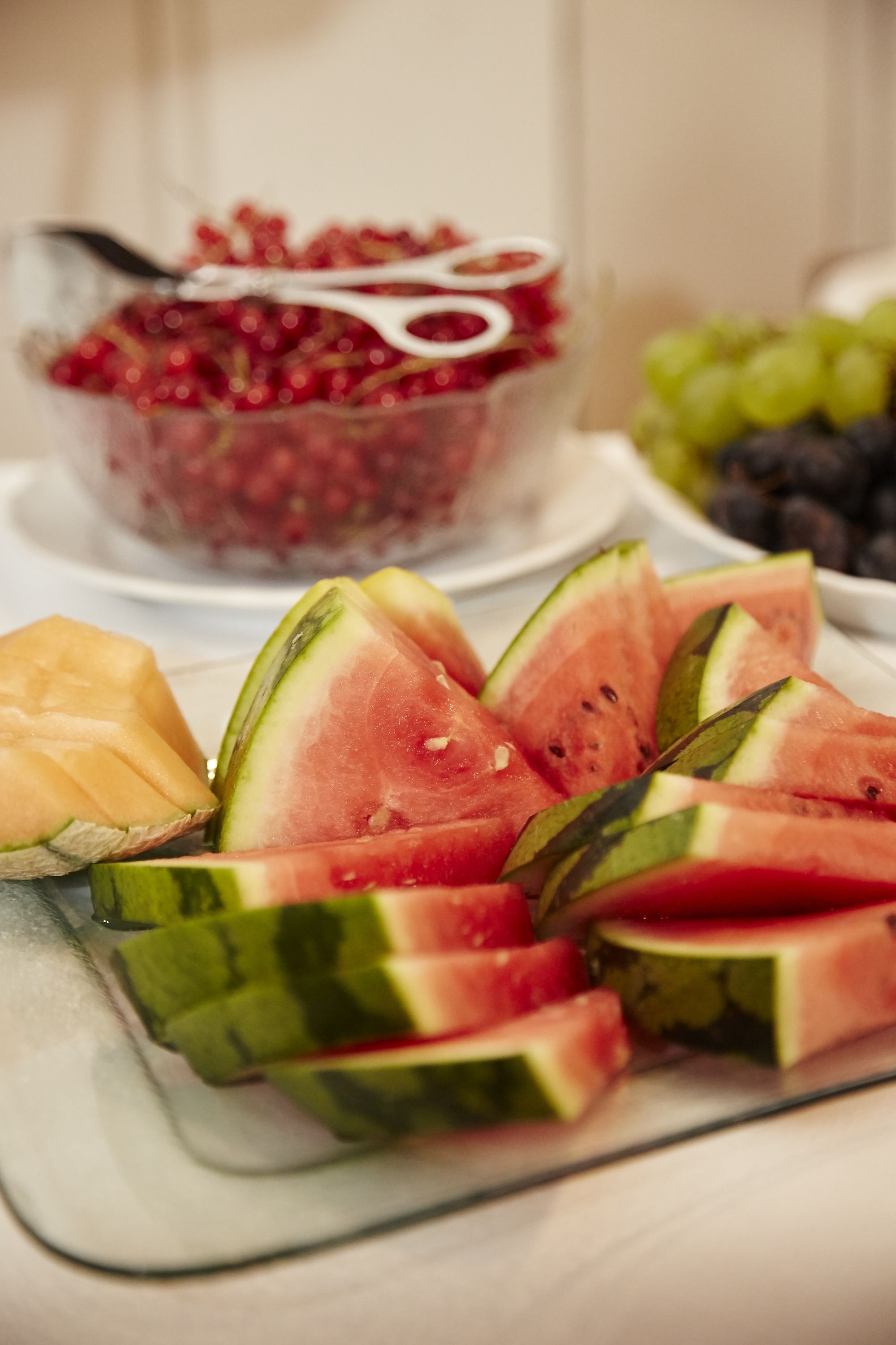 Una mesa con sandía en rodajas, melón, un bol de uvas y un recipiente con cerezas.