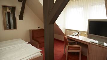 A hotel room with a bed, a desk with a chair, a television, and a window with curtains.