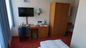 Una habitación de hotel con cama, escritorio con computadora, televisor, lámpara y armario.