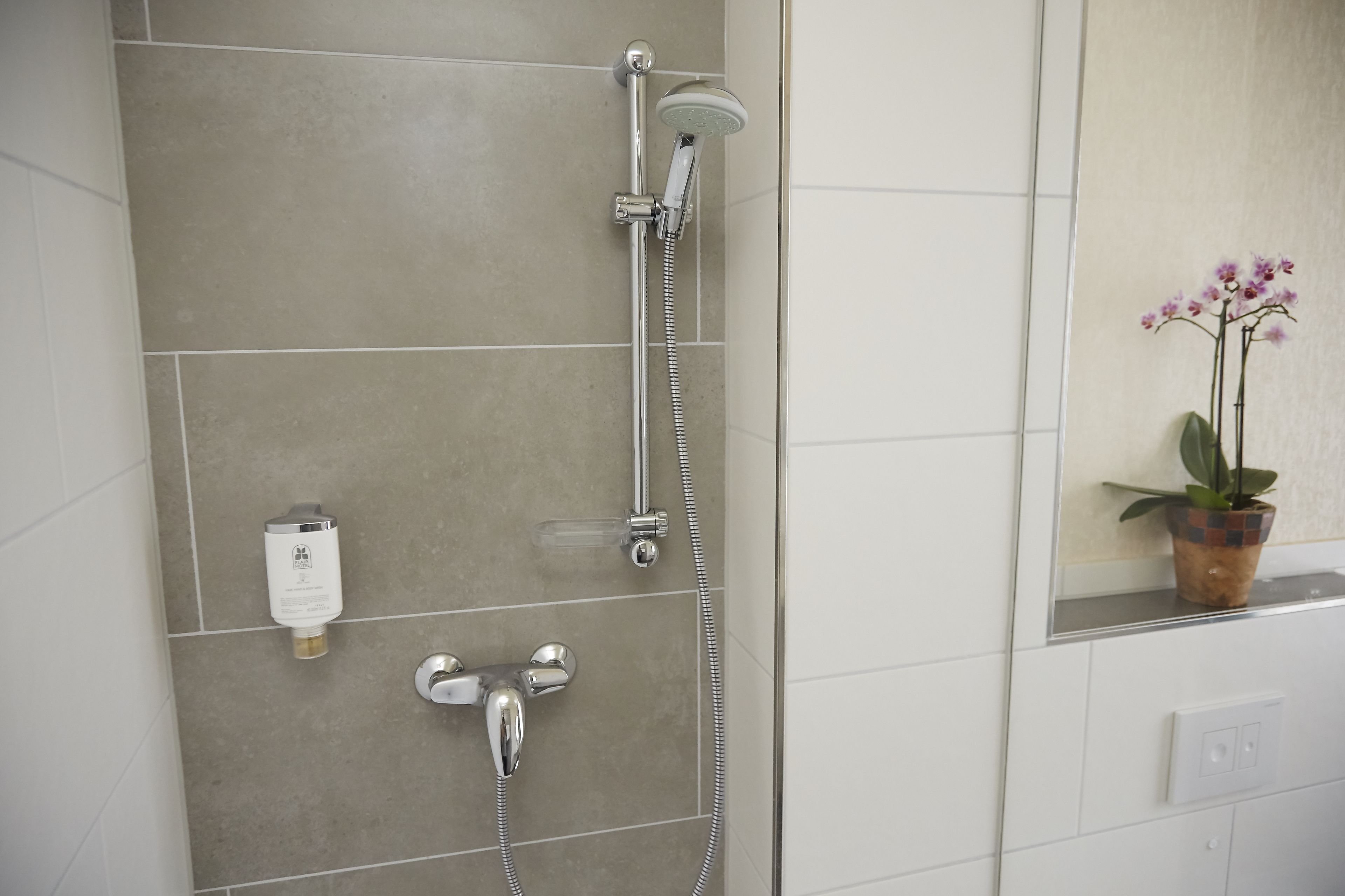 A bathroom with a shower, a towel rack, and a potted orchid.