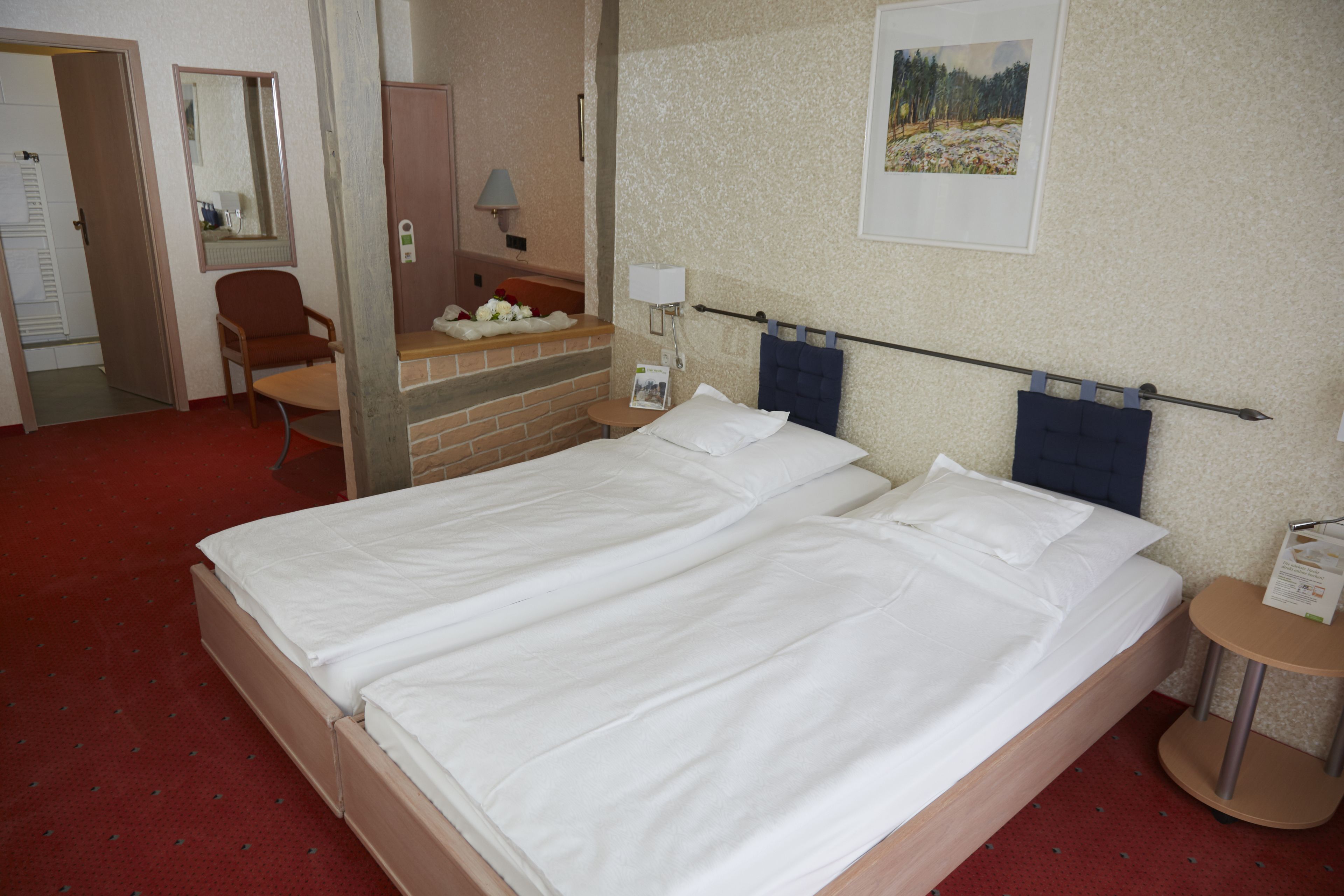 A hotel room with a large bed, a chair, a desk, and a mirror.