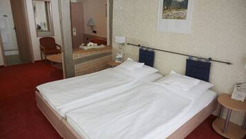 A hotel room with a large bed, a chair, a desk, and a mirror.