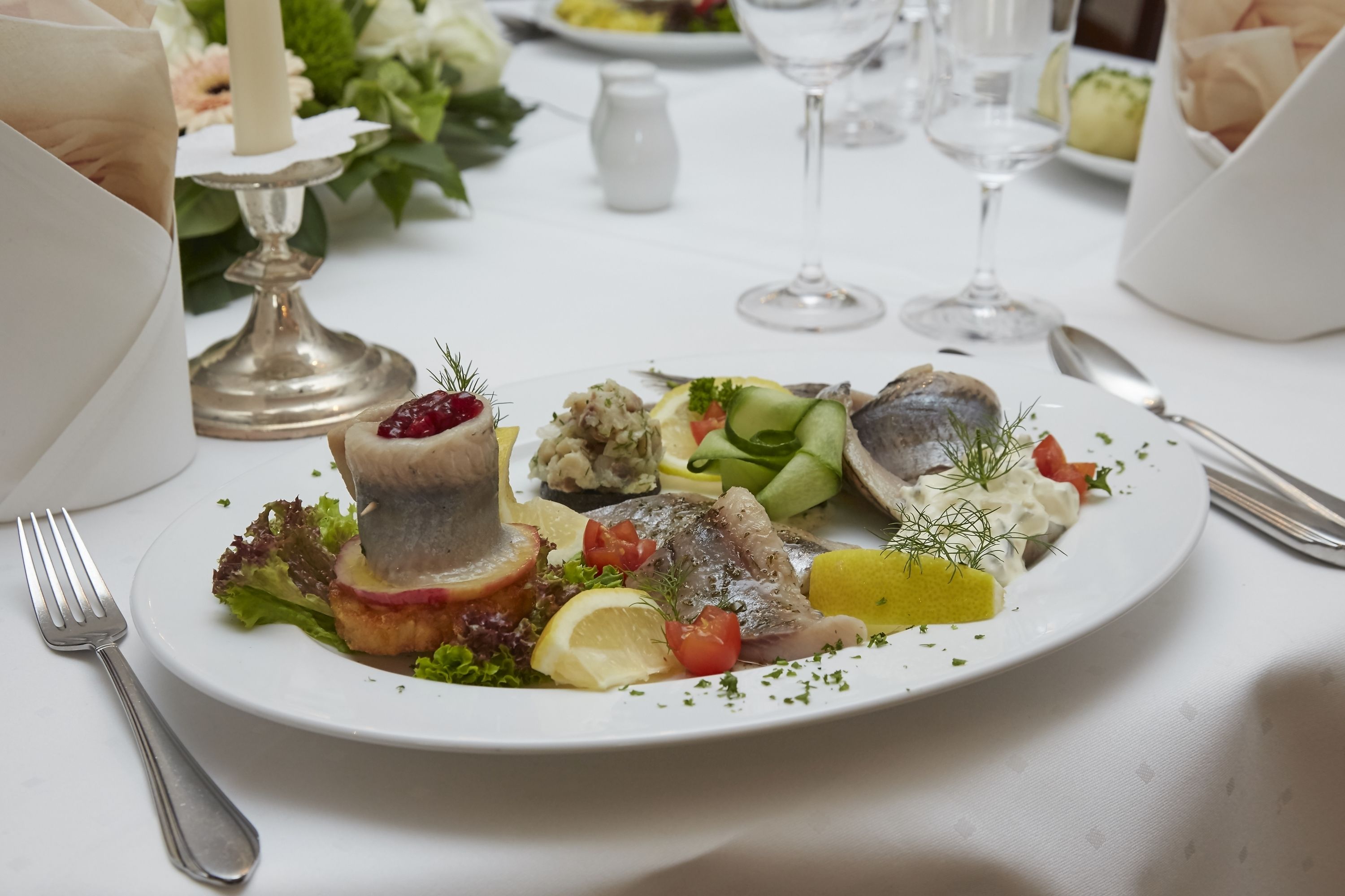 Un plato blanco con diversos mariscos y verduras, una vela y un salero sobre una mesa.