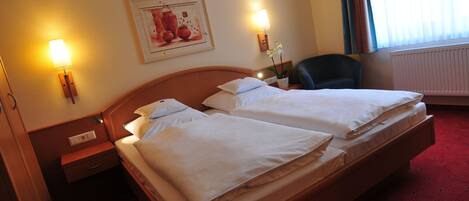 A hotel room with two beds, a nightstand, a lamp, a chair, and a painting on the wall.