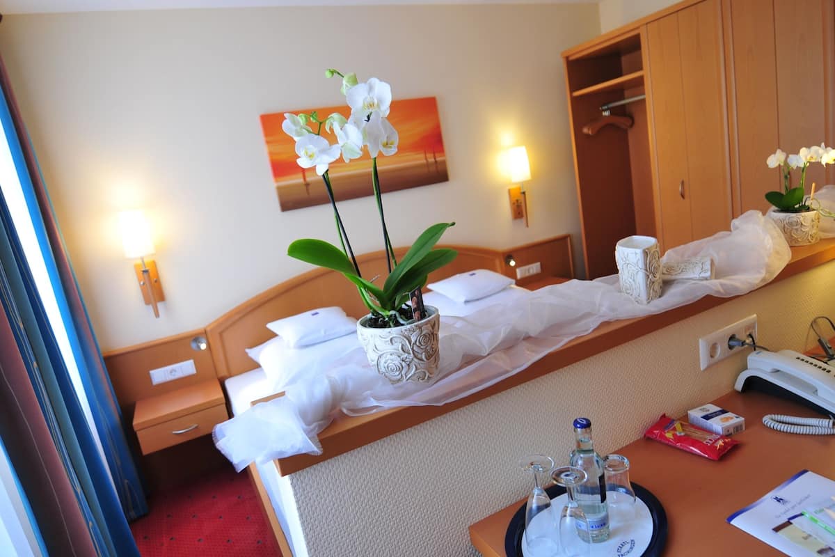 Une chambre d’hôtel avec un lit, une table de chevet avec une lampe, un miroir, une armoire et un tableau au mur.
