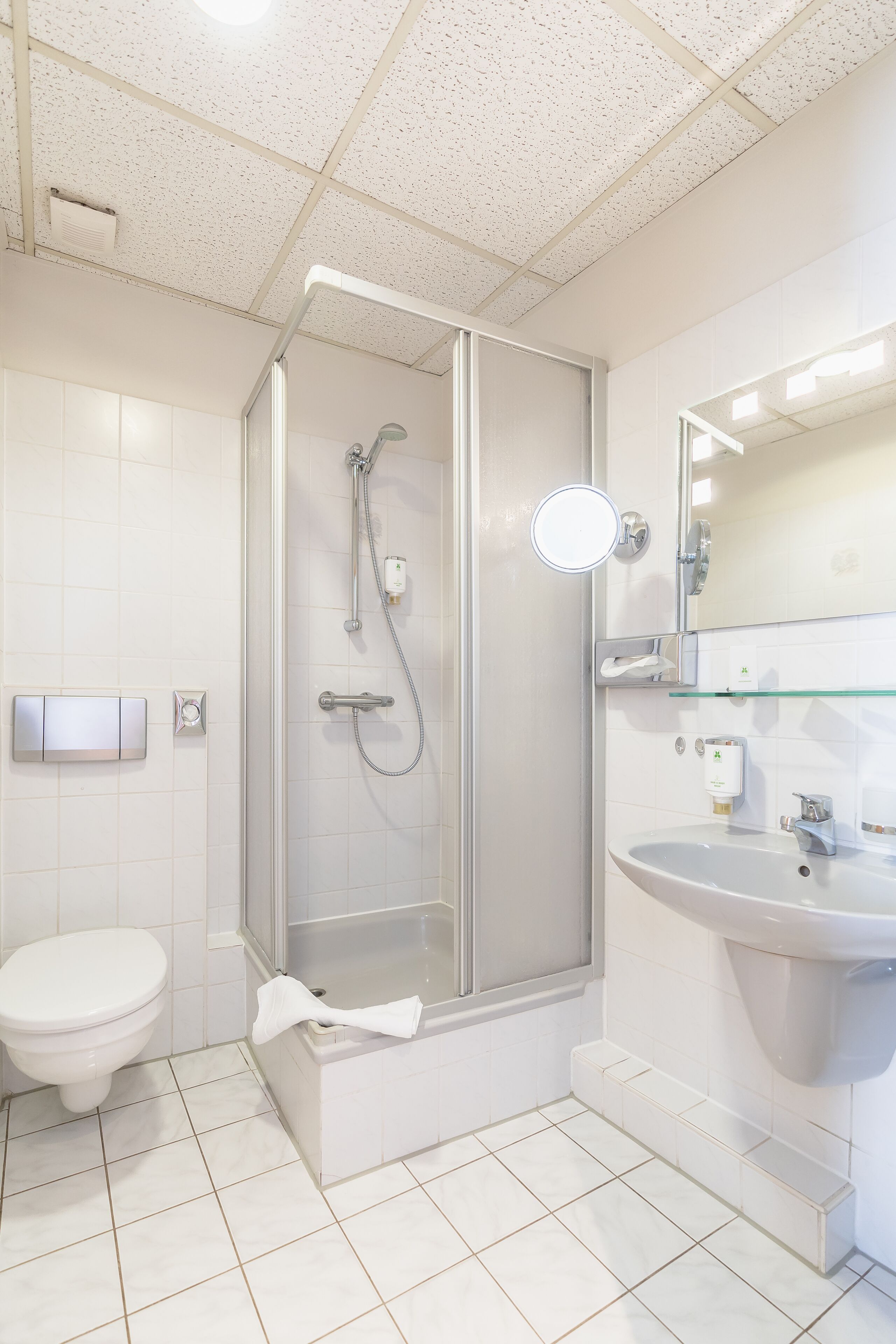 Un baño moderno con ducha de vidrio, un lavabo blanco y un inodoro.