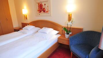 A hotel room with a double bed, a nightstand with a lamp, a chair, and a wall-mounted artwork.