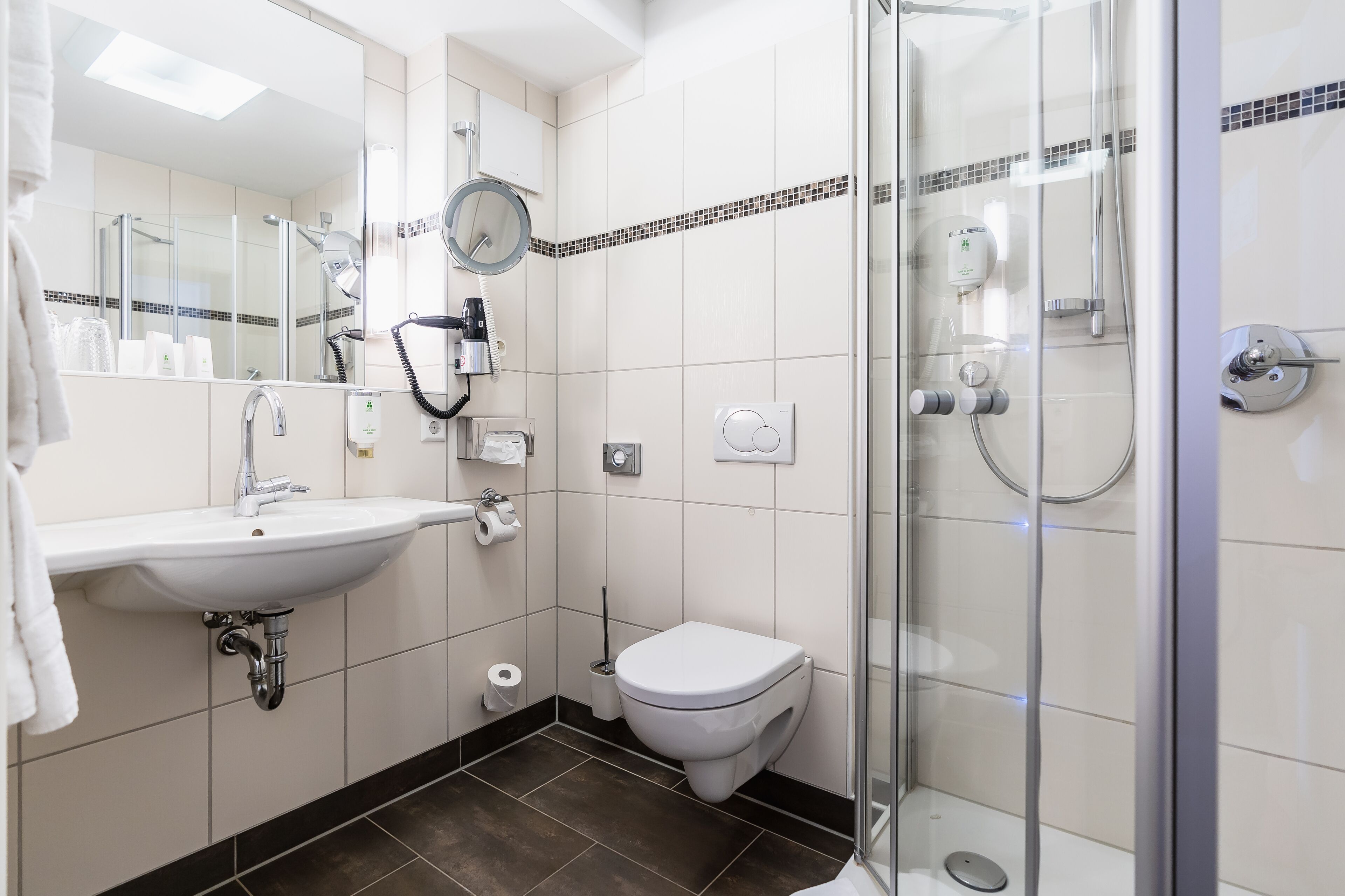 Een moderne badkamer met een wit wastafel, toilet en douchecabine met glazen wanden.