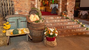A rustic brick building with a wooden barrel, a wheelbarrow with vegetables, and a sack of flowers. - Flair Hotel Deutsches Haus (Arendsee)
